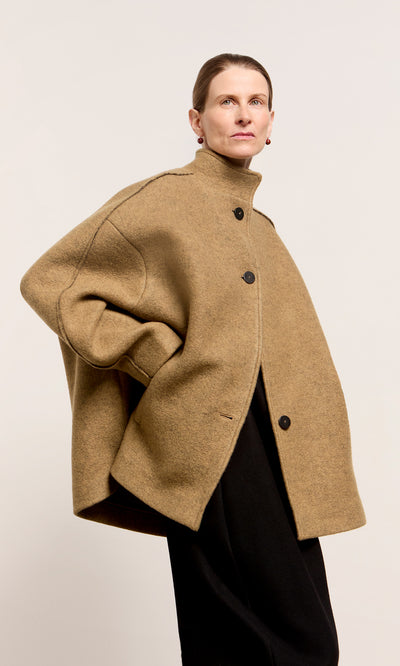 Plümo  Model in the Kilmore Coat: acorn brown wool, black buttons, high collar, set against a light background.