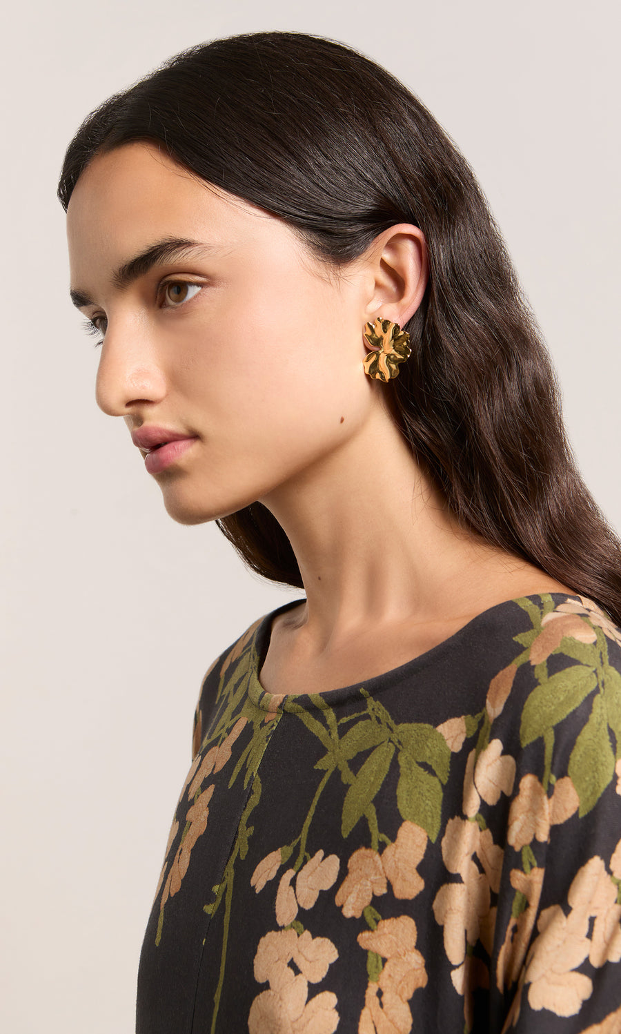 Plümo  Woman with long dark hair in floral top wears Klara Earrings - Gold, bold organic form, facing left.