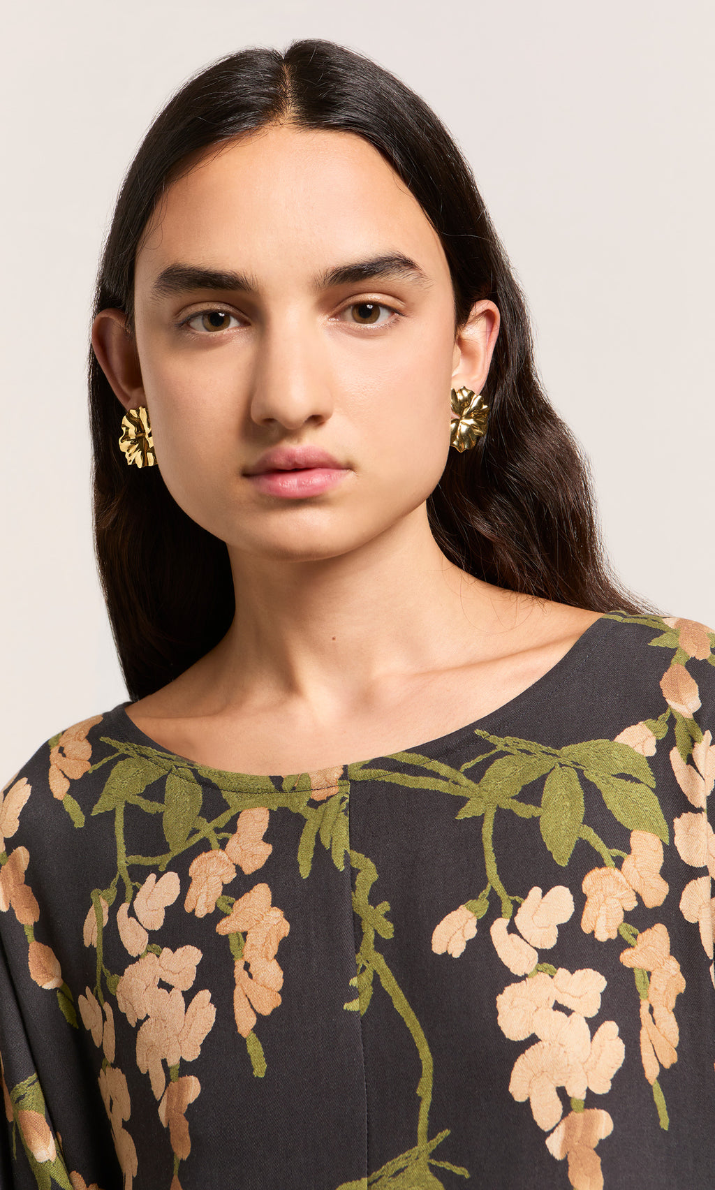 Plümo  Woman with long dark hair, gold floral earrings, and the Whisteria Dress featuring pink and green botanical print.