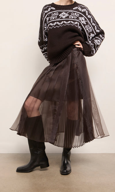 Plümo  Person in a black and white sweater, Kyffin Organza Skirt, and black boots stands indoors.