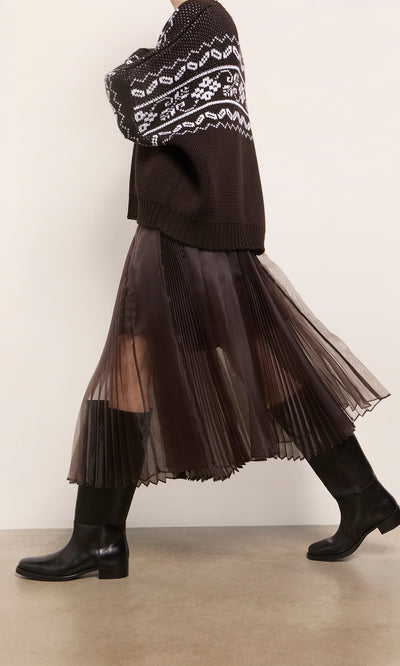 Plümo  Person in a black-and-white sweater, Kyffin Organza Skirt, and black boots walking indoors on a light brown floor.