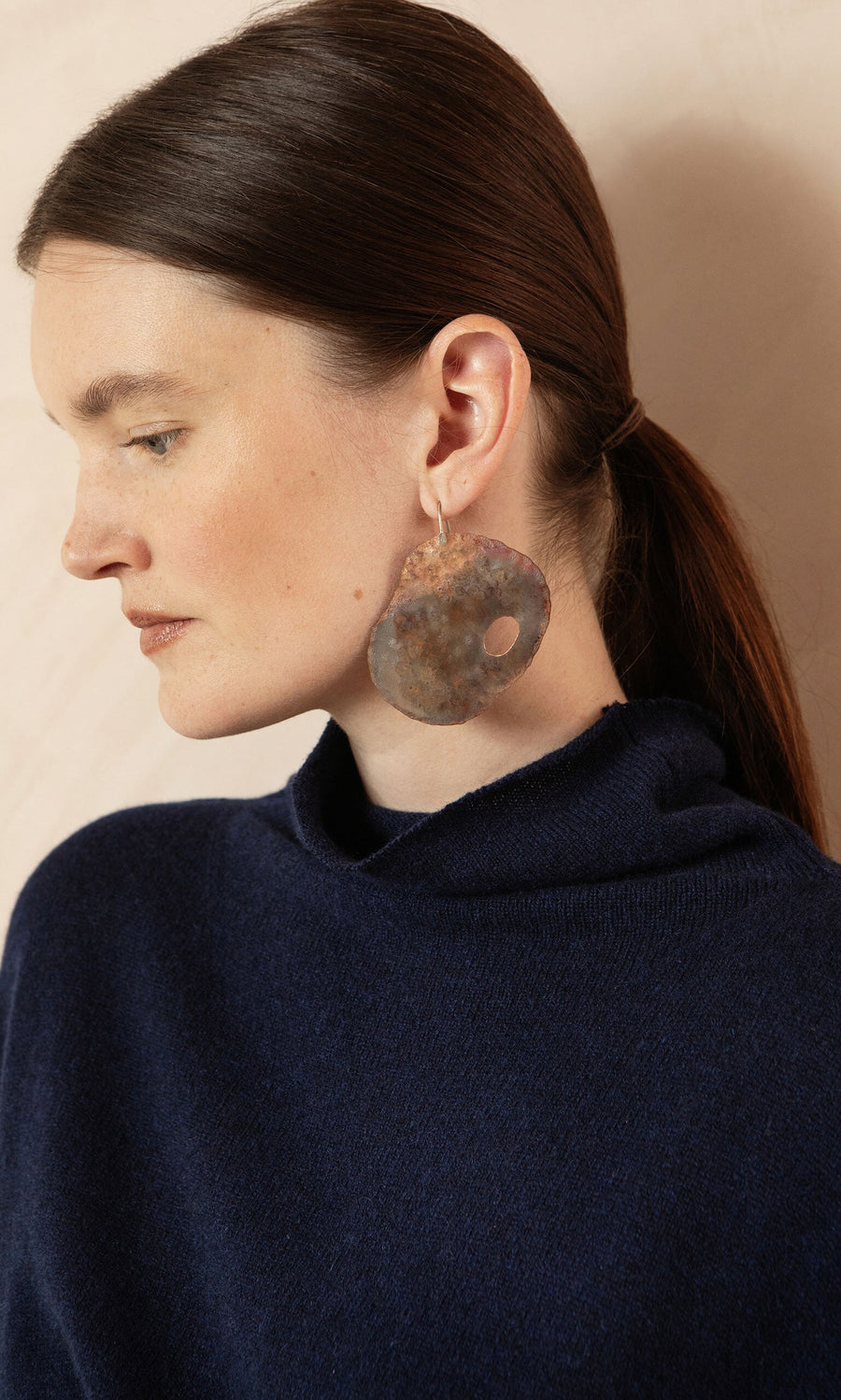 Plümo- Woman in a navy blue sweater wears Large Chroma Earrings with her brown hair pulled back.