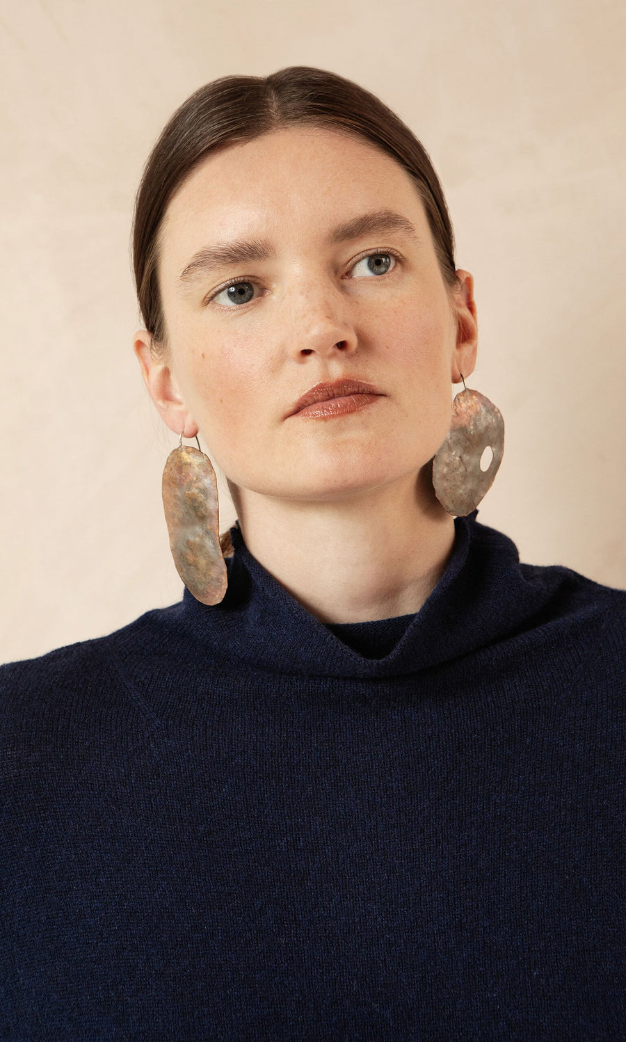 Plümo- Woman with straight brown hair in a dark blue sweater wearing Large Chroma Earrings, looking slightly to the side.
