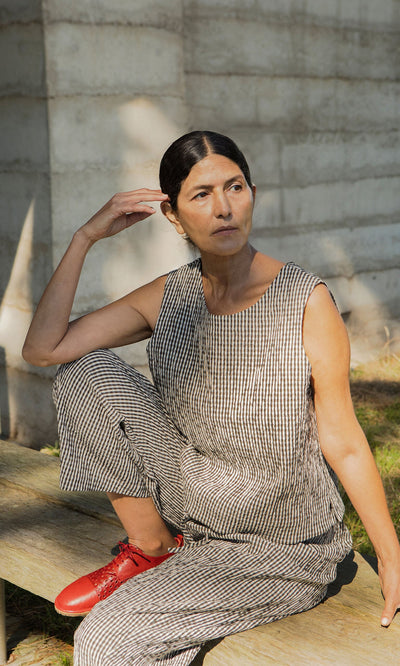 Plümo- Woman wears the Linda Top - Gingham, a seersucker cotton scoop neck, sitting outdoors on a bench. Made in London.