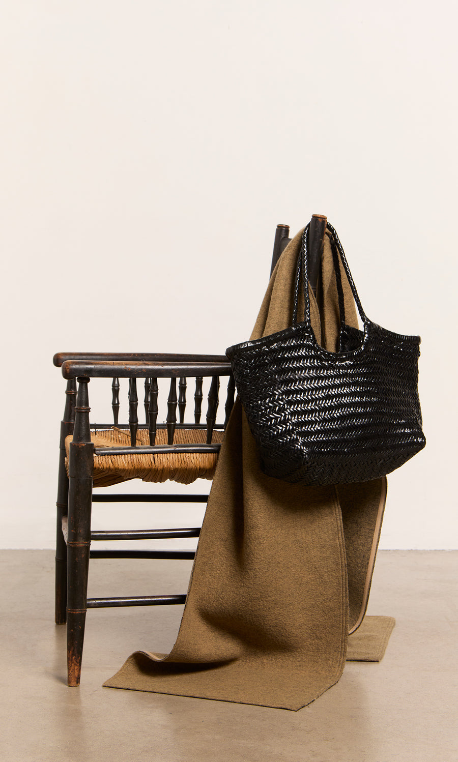 Plümo  A black Lyle Bag and a brown blanket rest on a rustic wooden chair atop a plain floor.