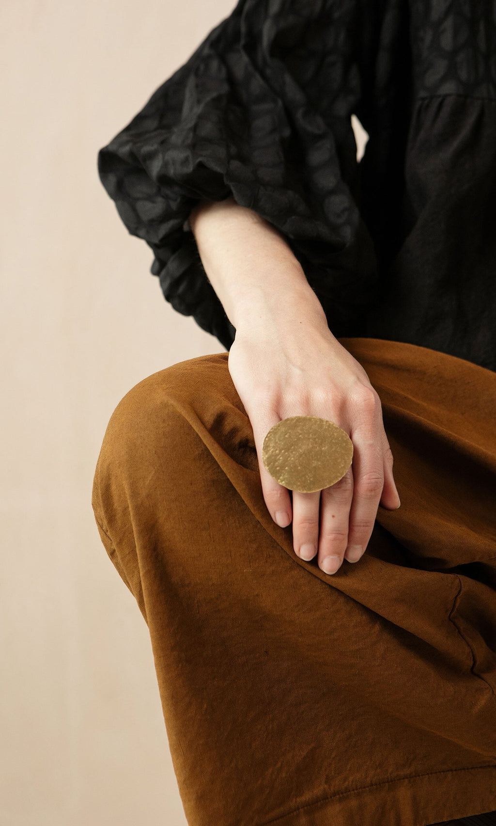 Plümo- A person wearing brown pants shows off the large Margot Ring as they rest their hand on their knee.