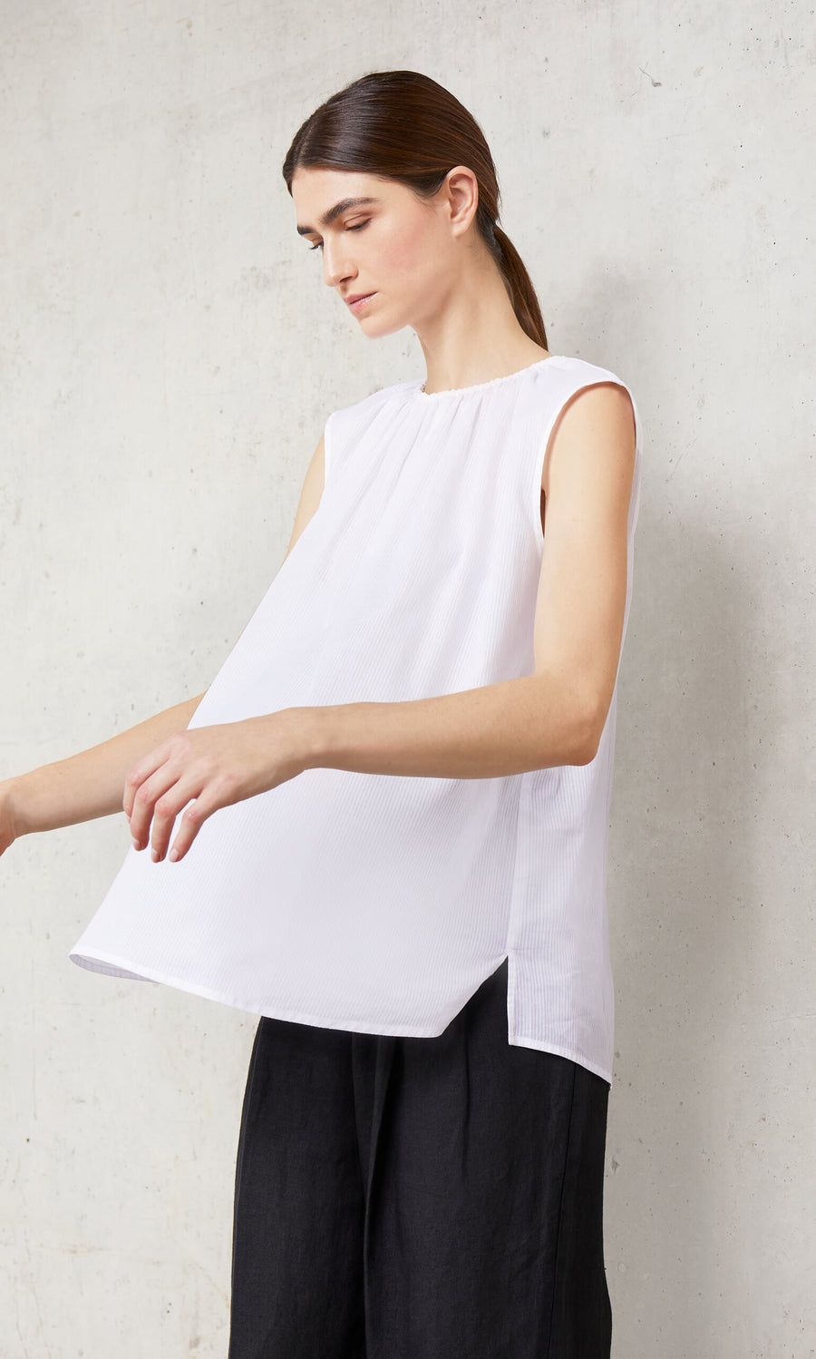 Plümo- A person in the Marie Top - White and black pants stands against a light textured wall, looking down.