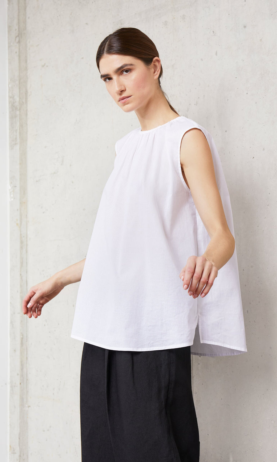 Plümo- A person in the Marie Top - White and black pants stands against a light-colored concrete wall.