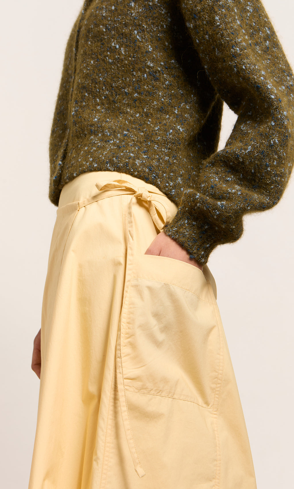Plümo- Person wearing a textured olive sweater and the Marigold Wrap Skirt, a high-waisted cotton poplin skirt with tie detail.