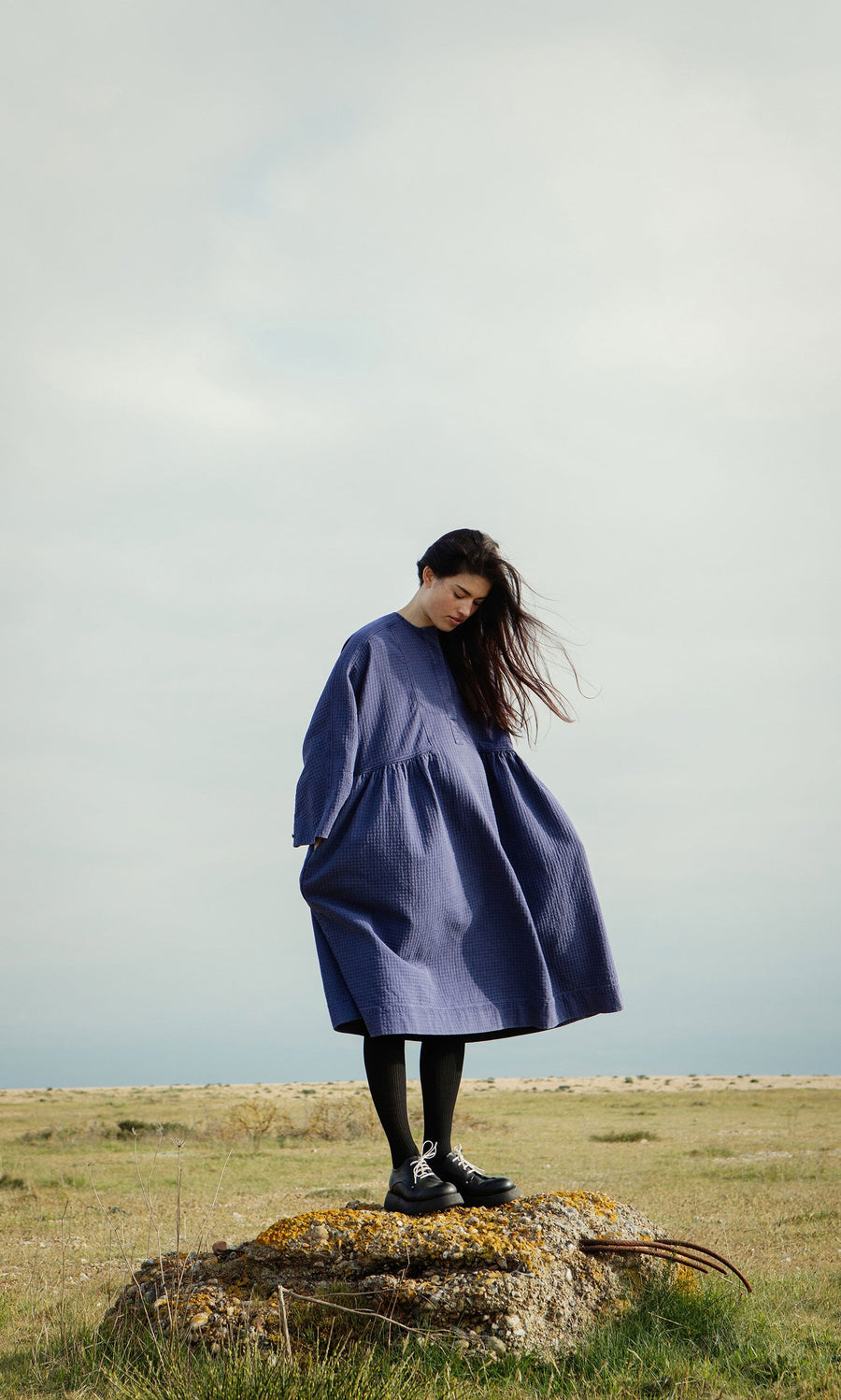 Plümo- Woman in a loose blue dress stands on a rock wearing Hosier Brogues, handcrafted in Italy.