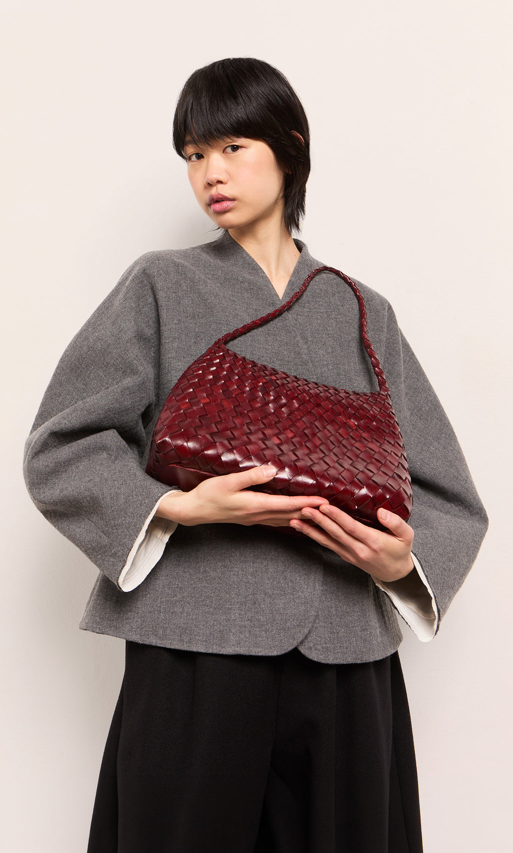 Plümo  Person in gray jacket holding the Moone Bag, a hand-woven leather bag from South Africa, on a plain light background.