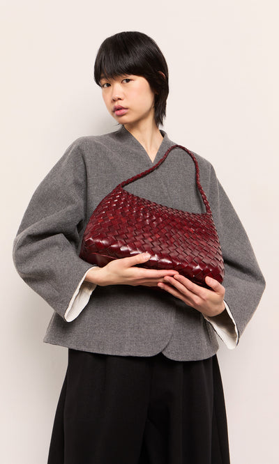 Plümo  Person in gray jacket holding the Moone Bag, a hand-woven leather bag from South Africa, on a plain light background.