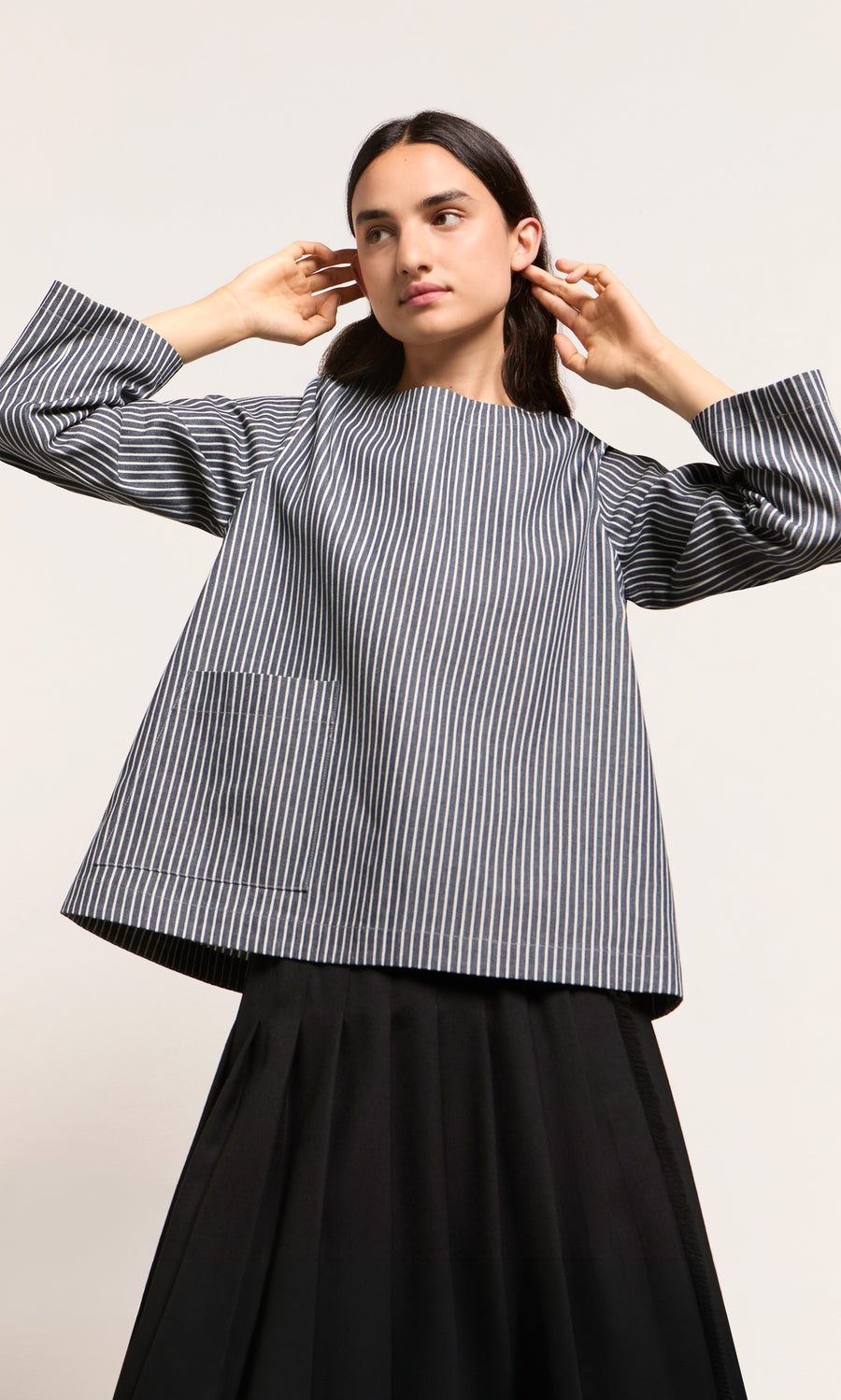 Plümo  Person in a Norfolk Top and black skirt poses with hands near head against a plain background.