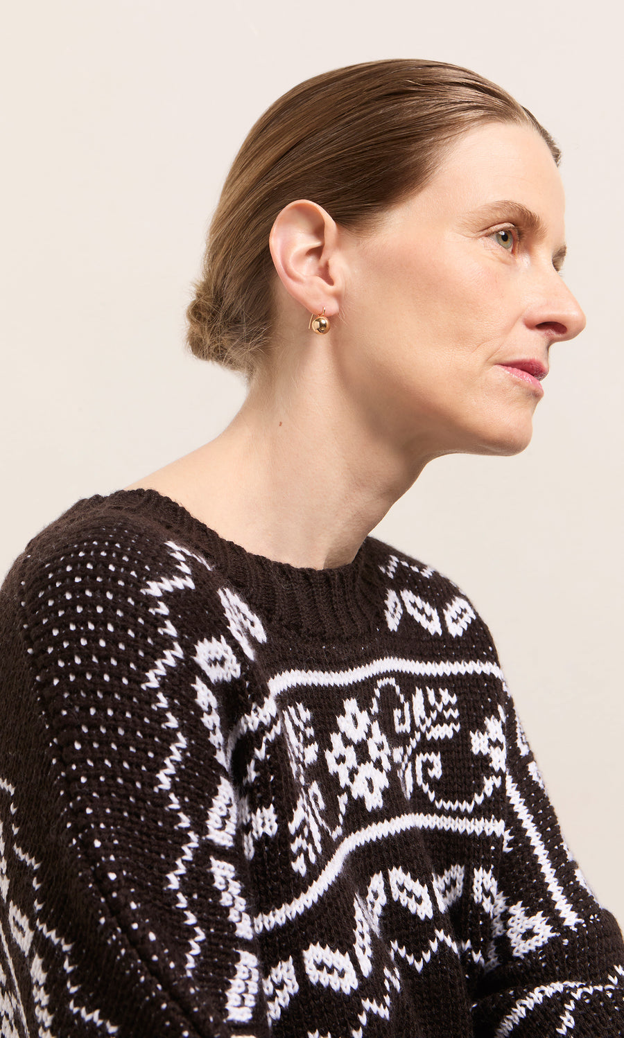 Plümo  Woman in profile wears Ora Earrings, black and white sweater, hair tied back, on a neutral background.
