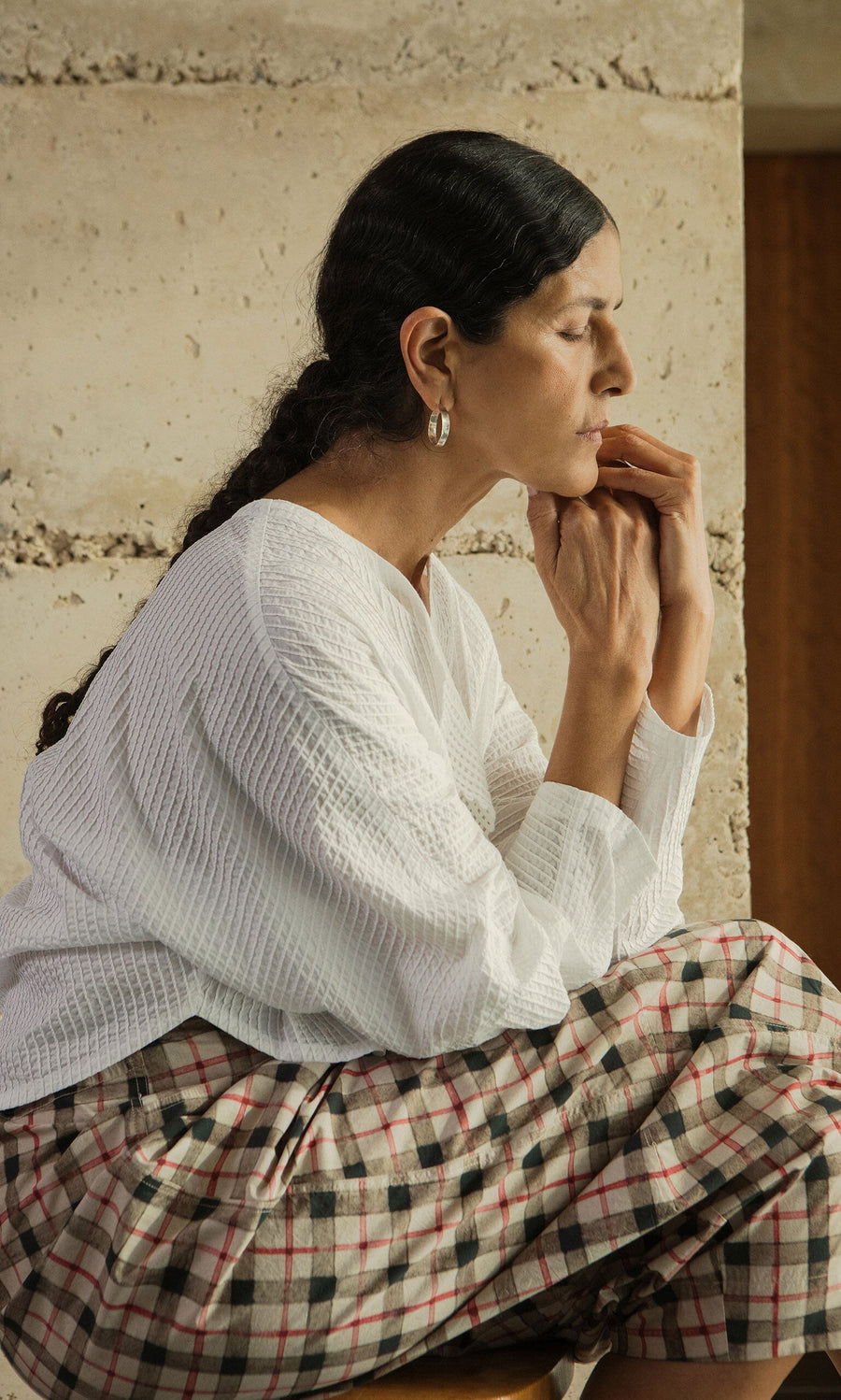 Plümo- A woman with dark braided hair models Hui Hoops silver earrings, resting her chin on her hands in a white top.