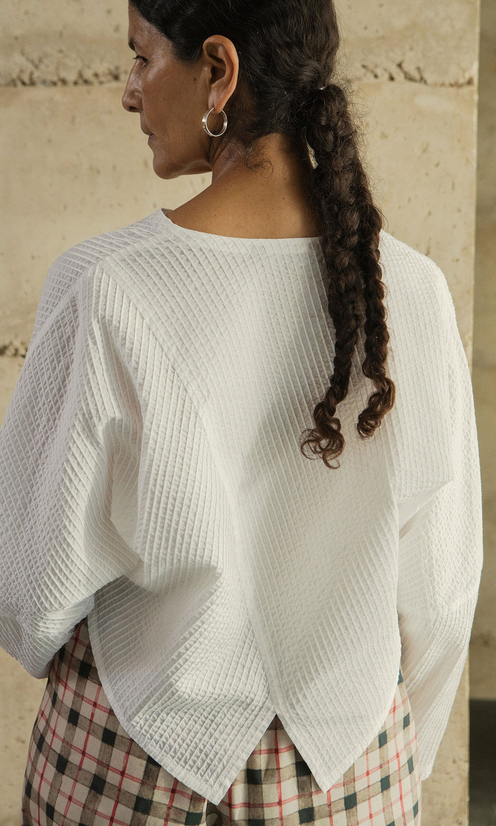 Plümo- Woman with a braided ponytail in the Orna Pleat Jacket, cocoon silhouette, and plaid skirt, shown from the back.