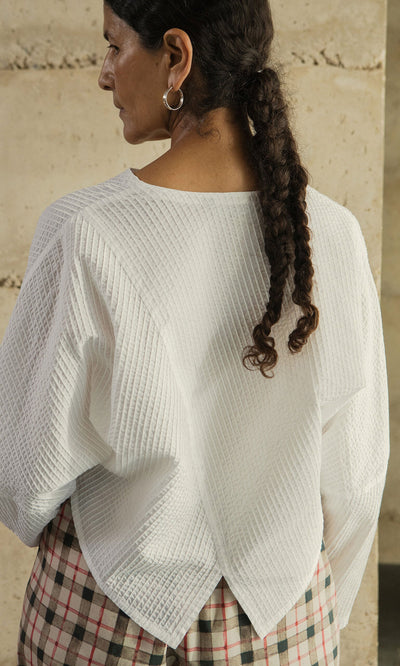 Plümo- Woman with a braided ponytail in the Orna Pleat Jacket, cocoon silhouette, and plaid skirt, shown from the back.