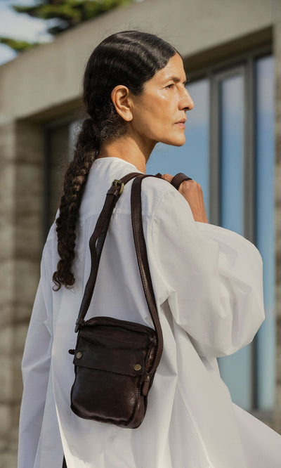 Plümo- Woman with long dark hair in a white shirt carries an Orton Parcel Bag outdoors.