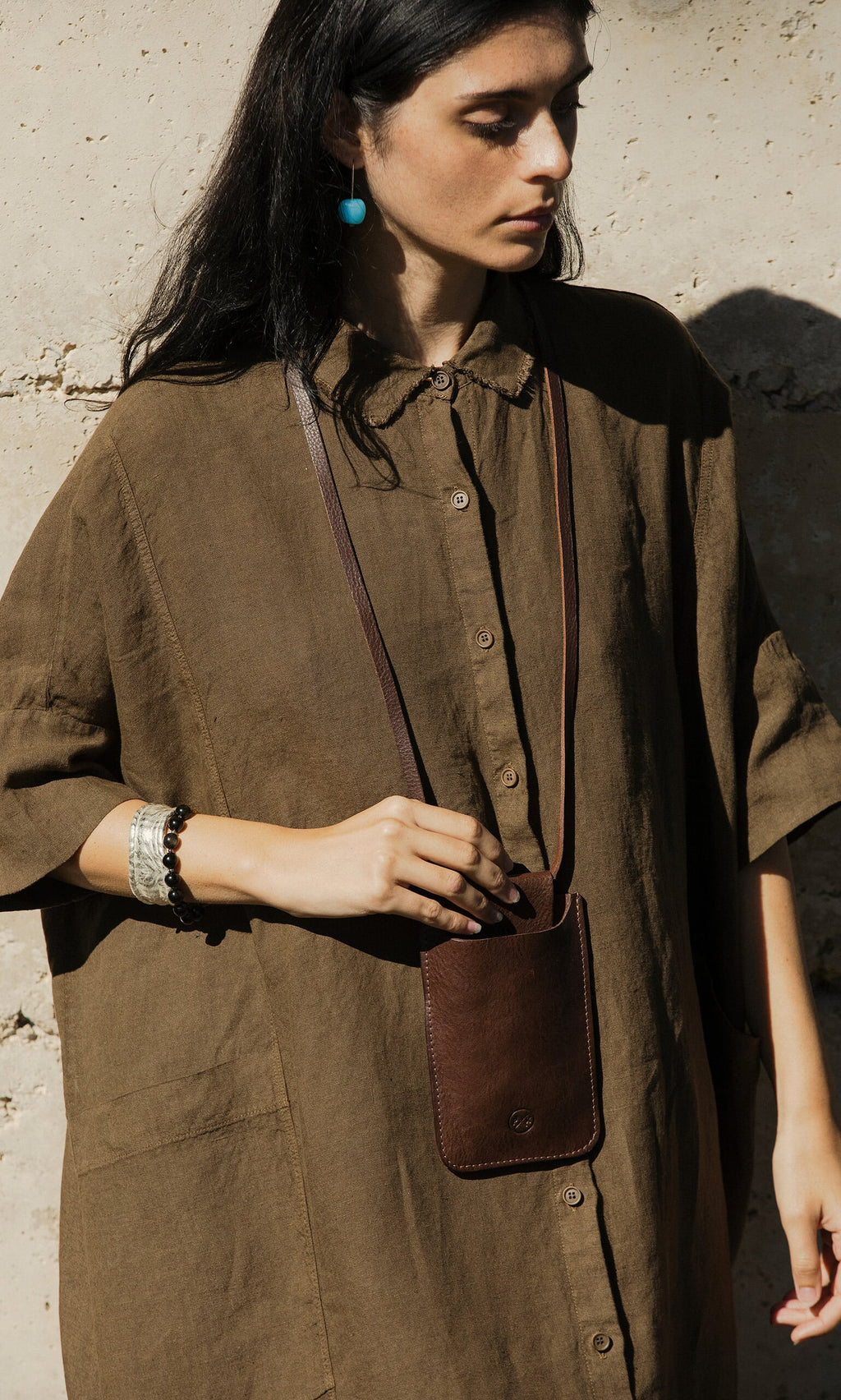 Plümo- Woman in a loose brown shirt dress with the Purdy Bag, a silver bracelet, and turquoise earring.
