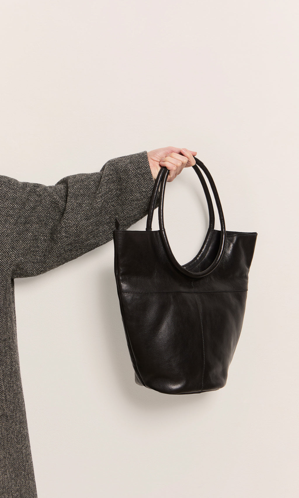 Plümo  Person in a gray coat holding the Oval Shoulder Bag by its handles against a light background.