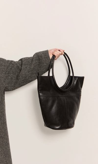 Plümo  Person in a gray coat holding the Oval Shoulder Bag by its handles against a light background.