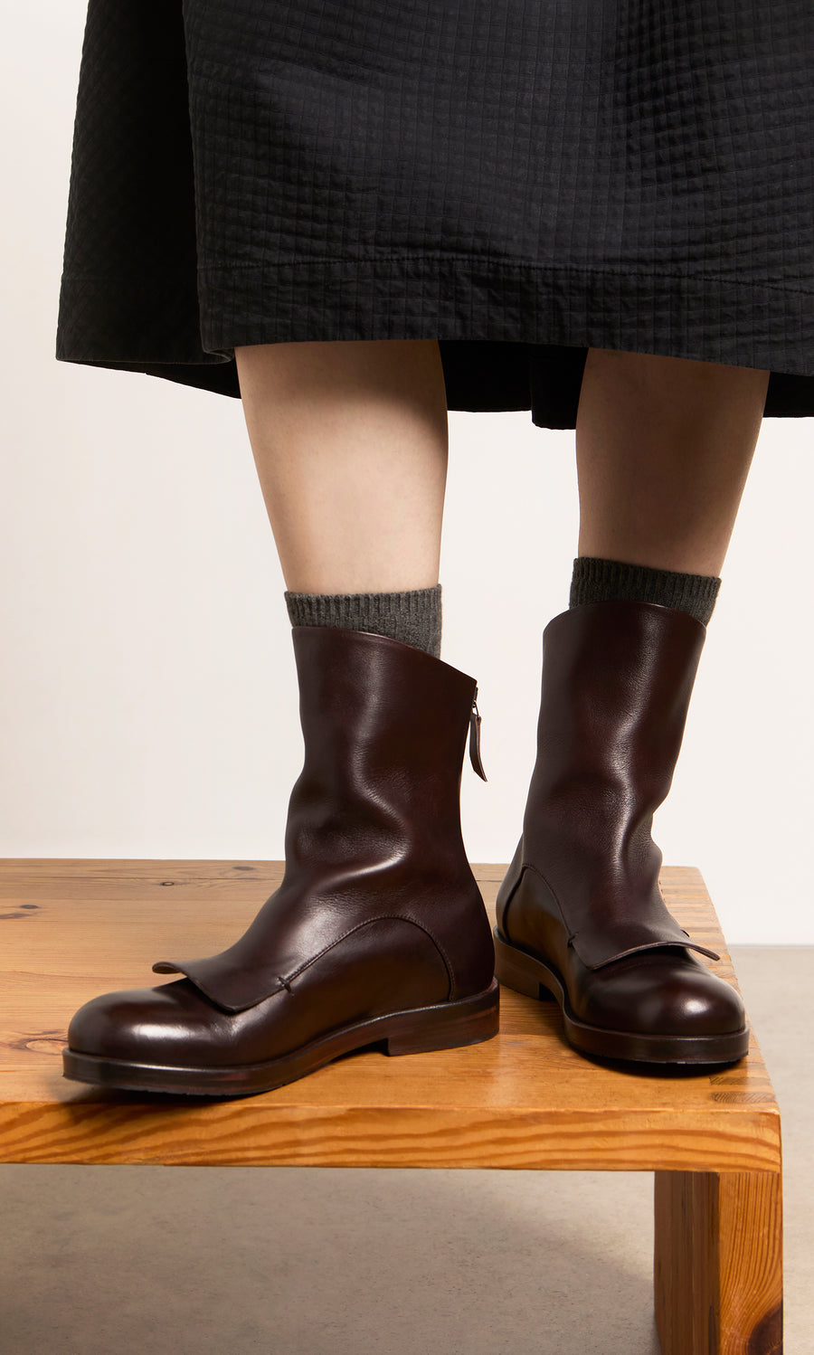 Plümo  Person in Over Boots and gray socks, standing on a bench, black skirt visible; artisan-made in Italy leather ankle boots.
