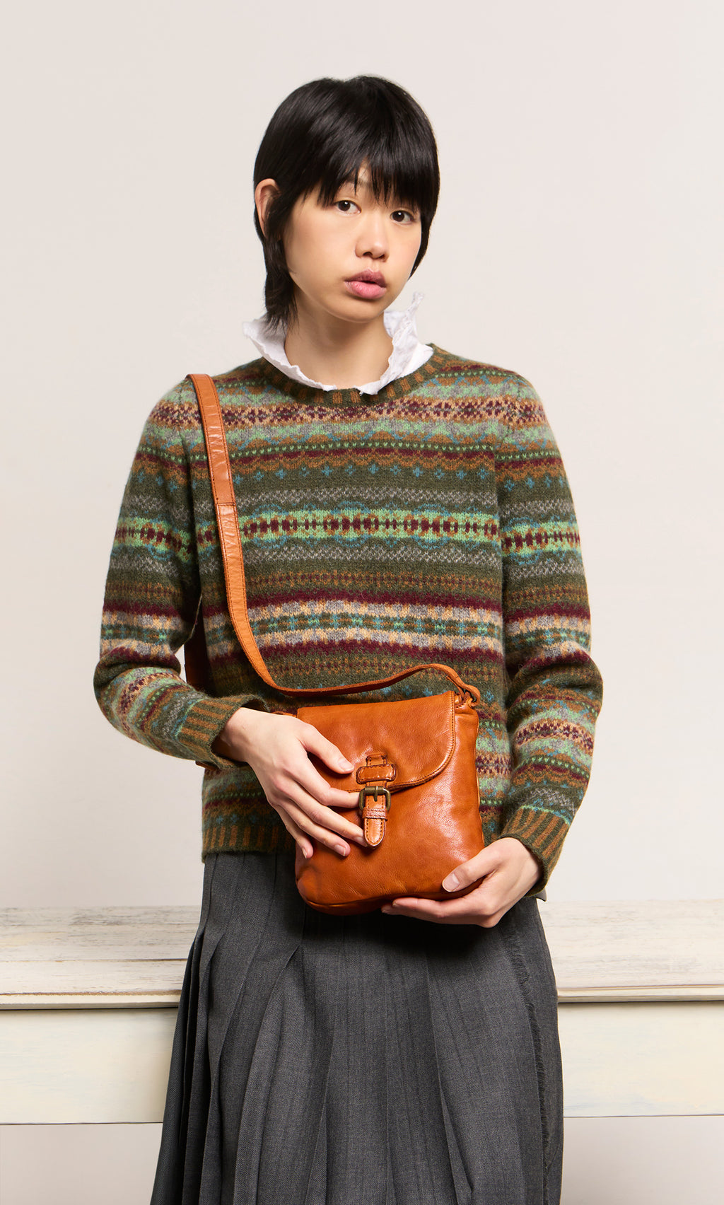 Plümo  Person in a patterned sweater and gray skirt holds a Parcel Bag - Chestnut, standing before a plain background.
