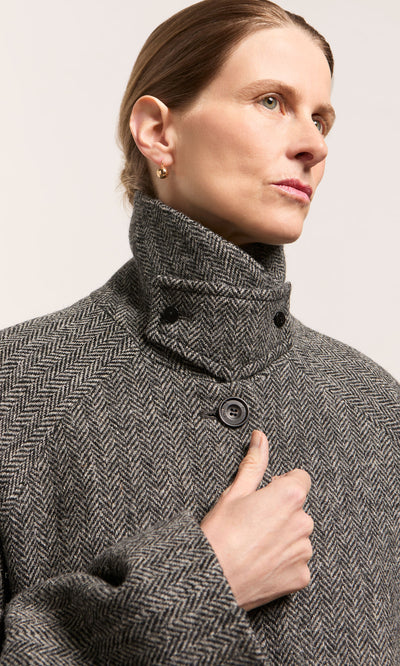 Plümo  Person in a gray herringbone coat wears Ora Earrings, gold drops, and looks to the side with a neutral expression.