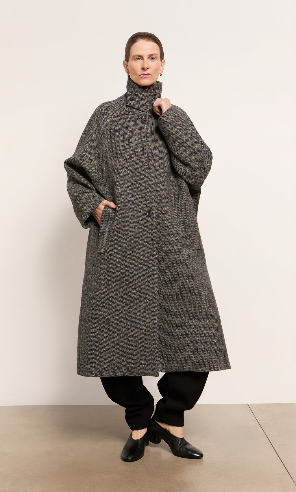 Plümo  Person wears a Balmacaan Tweed Coat made in England with black pants and shoes, set against a plain background.