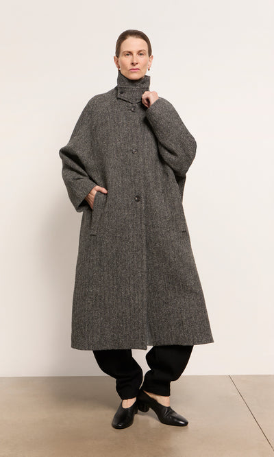 Plümo  Person wears a Balmacaan Tweed Coat made in England with black pants and shoes, set against a plain background.