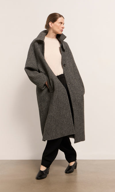 Plümo  Woman in Balmacaan Tweed Coat, beige top, black pants—classic heritage style against a plain background.