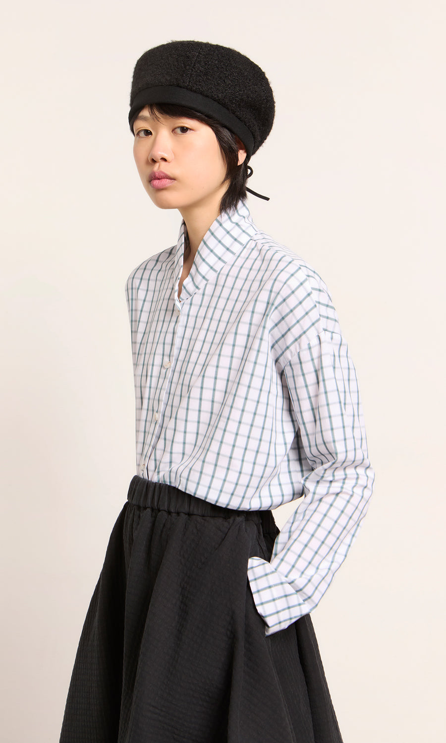 Plümo  Wearing a black hat, checked shirt, and skirt—showcasing the Perinne Beret, a handmade adjustable Parisian style.