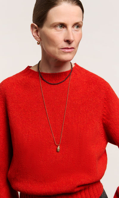 Plümo  Woman in a bright red sweater wears the Rowena Necklace and small earrings, looking to the side against a plain background.