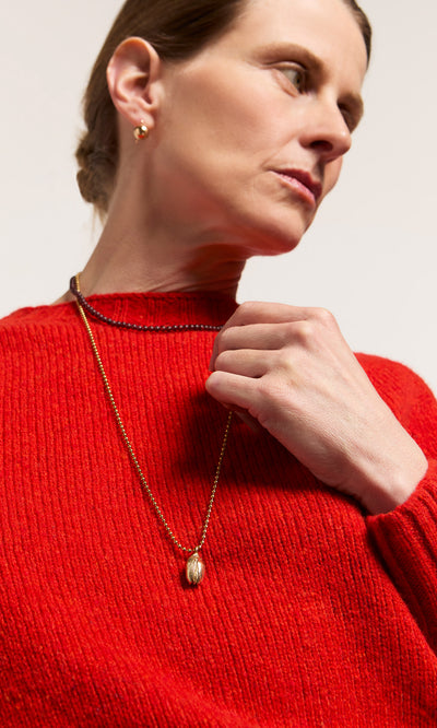 Plümo  Woman in a red sweater holds the Rowena Necklace, a sterling silver bead piece, gazing off to the side.