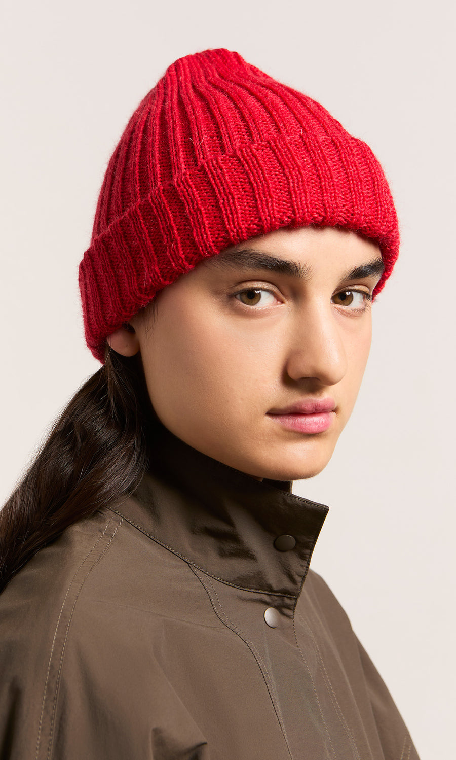 Plümo  Model in Red Breton Beanie and brown jacket, gazing to the side with a neutral expression.