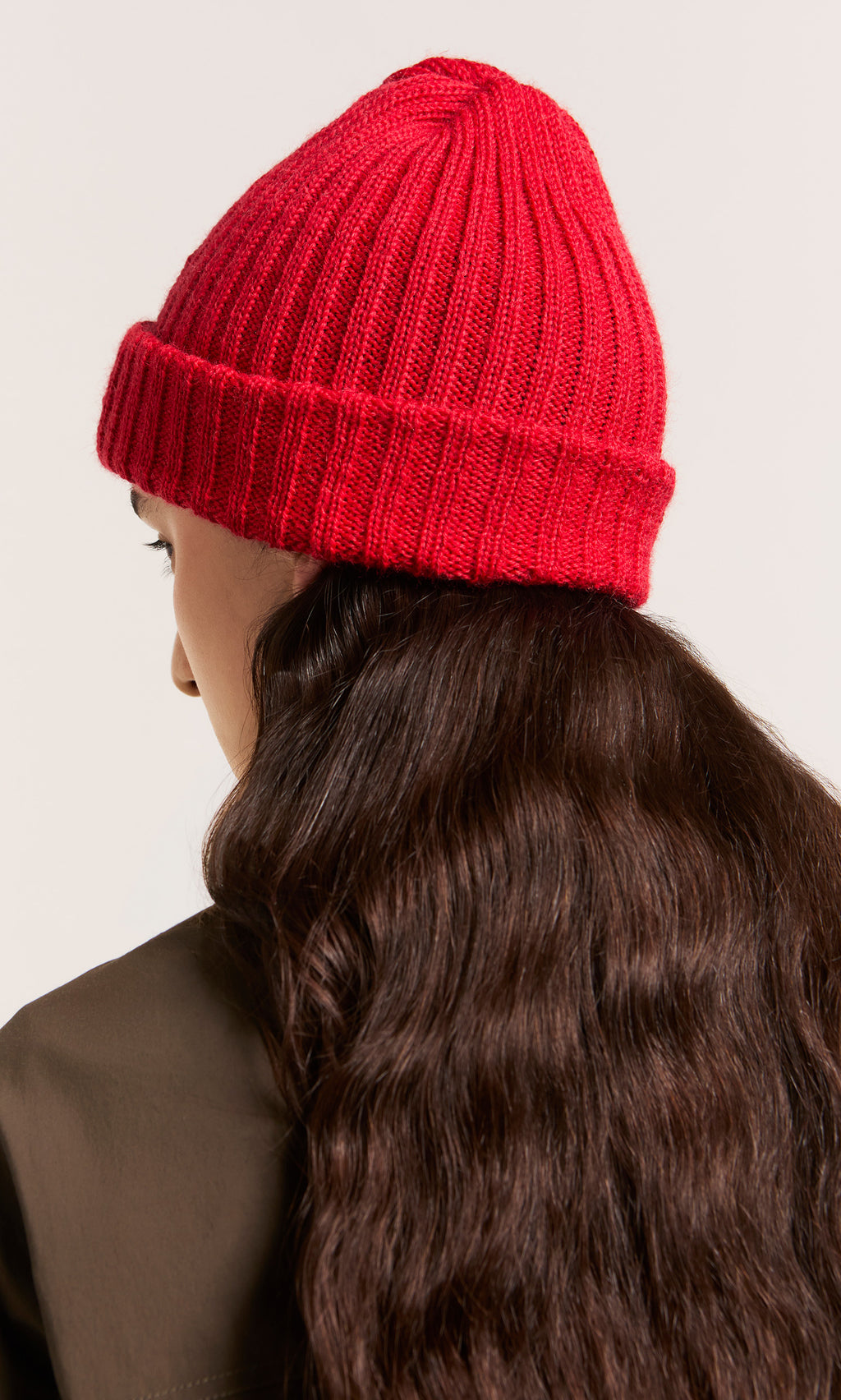 Plümo  Person with long wavy brown hair in a Red Breton Beanie, seen from behind against a light background.