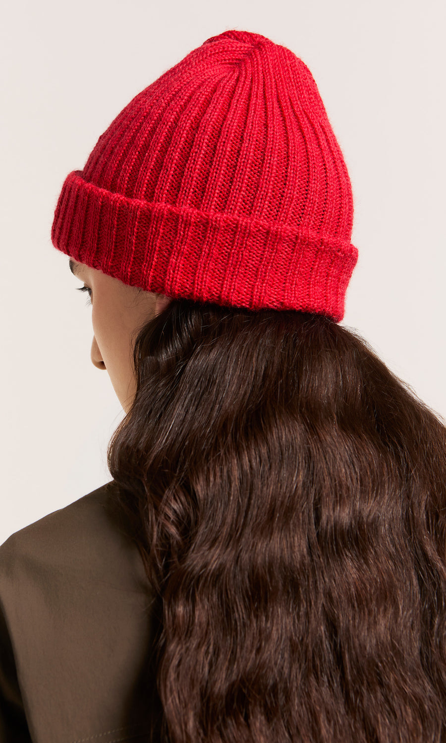 Plümo  Person with long wavy brown hair in a Red Breton Beanie, seen from behind against a light background.