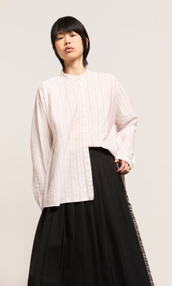 Plümo  Person in a loose Ejaz Shirt with embroidered stripes and a long black skirt stands against a plain, light background.