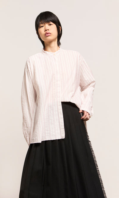 Plümo  Person in a loose Ejaz Shirt with embroidered stripes and a long black skirt stands against a plain, light background.