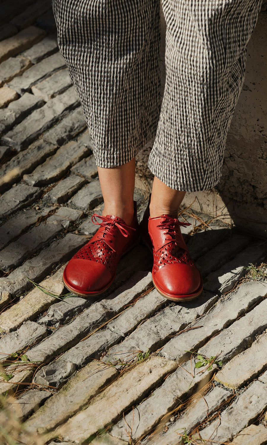 Plümo- Person wearing Magui Brogues and striped pants stands on a sunlit cobblestone path.