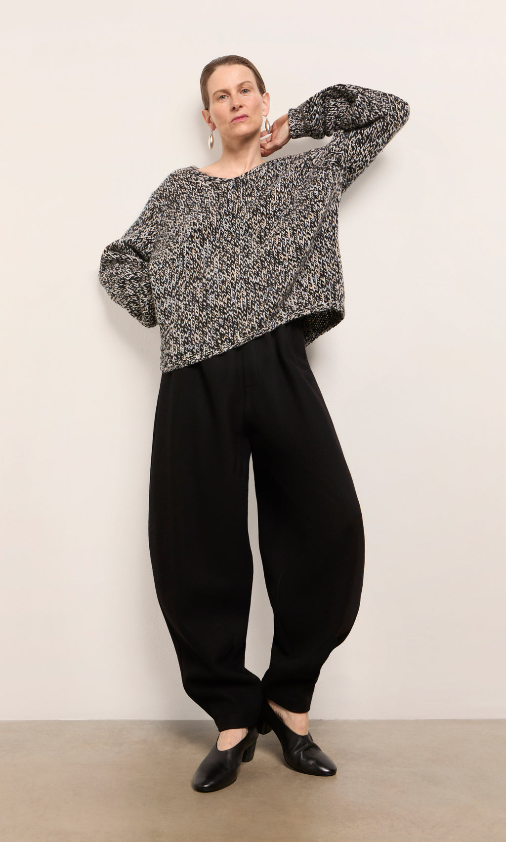 Plümo  Woman wearing Circle Pants - Boiled Black, a black and white sweater, and black shoes against a white wall.