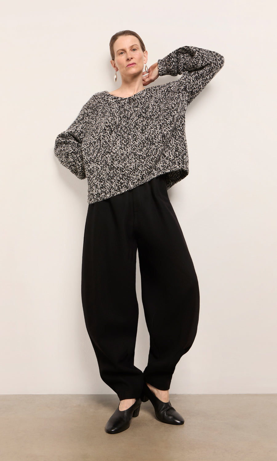 Plümo  Woman wearing Circle Pants - Boiled Black, a black and white sweater, and black shoes against a white wall.