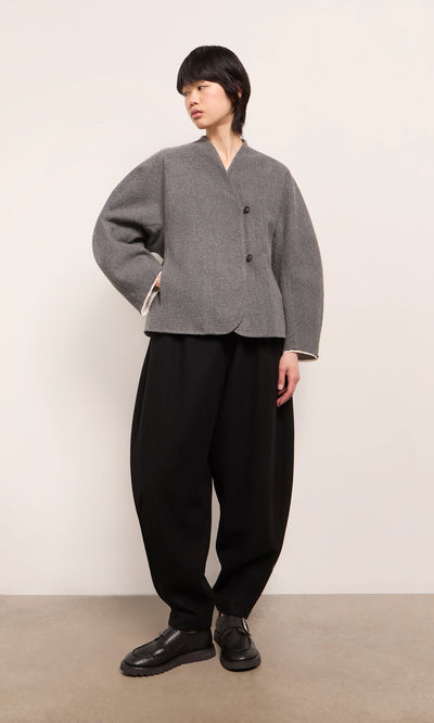 Plümo  Model wears Circle Pants - Boiled Black and a gray buttoned jacket, standing against a plain background.