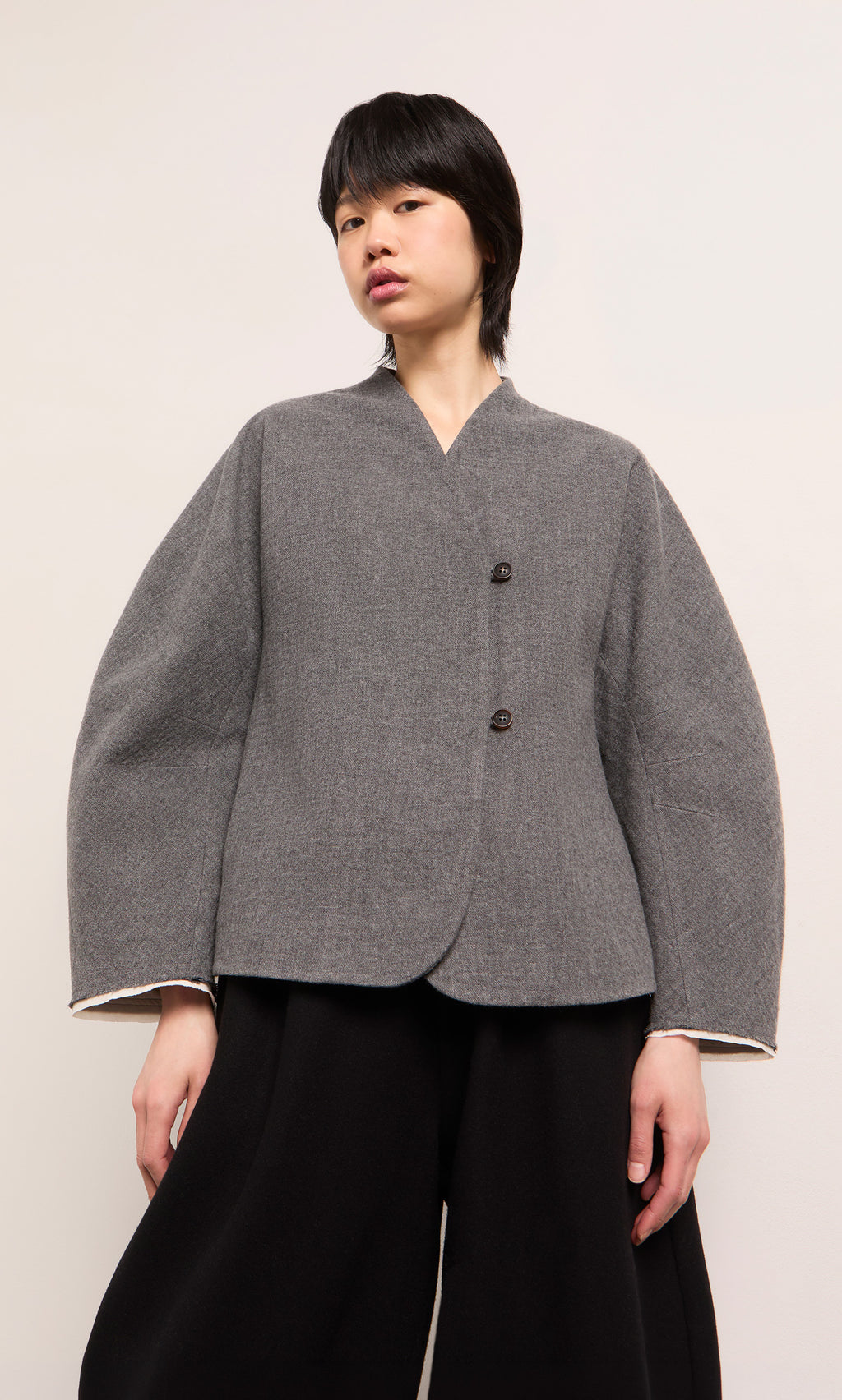 Plümo  Person wearing a grey Rostock Jacket with two buttons and wide black pants, standing against a plain background.
