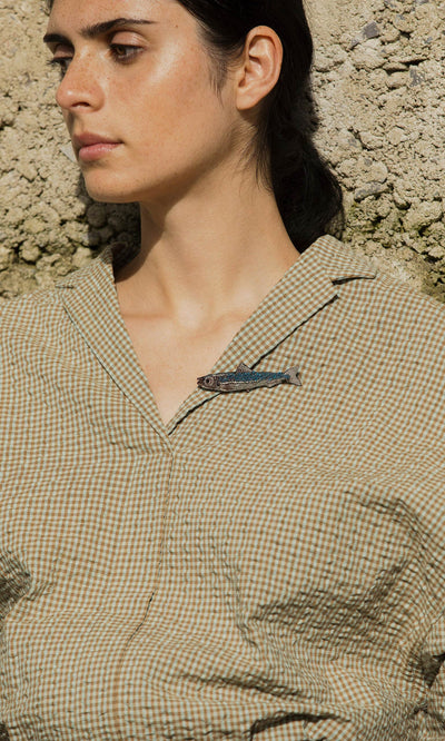Plümo- A person in a checked shirt wears the Sardine Brooch, standing against a textured wall.