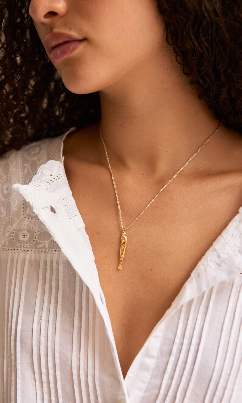 Plümo- A woman in a white blouse wears the Sardine Necklace; only her lower face and neck are visible.