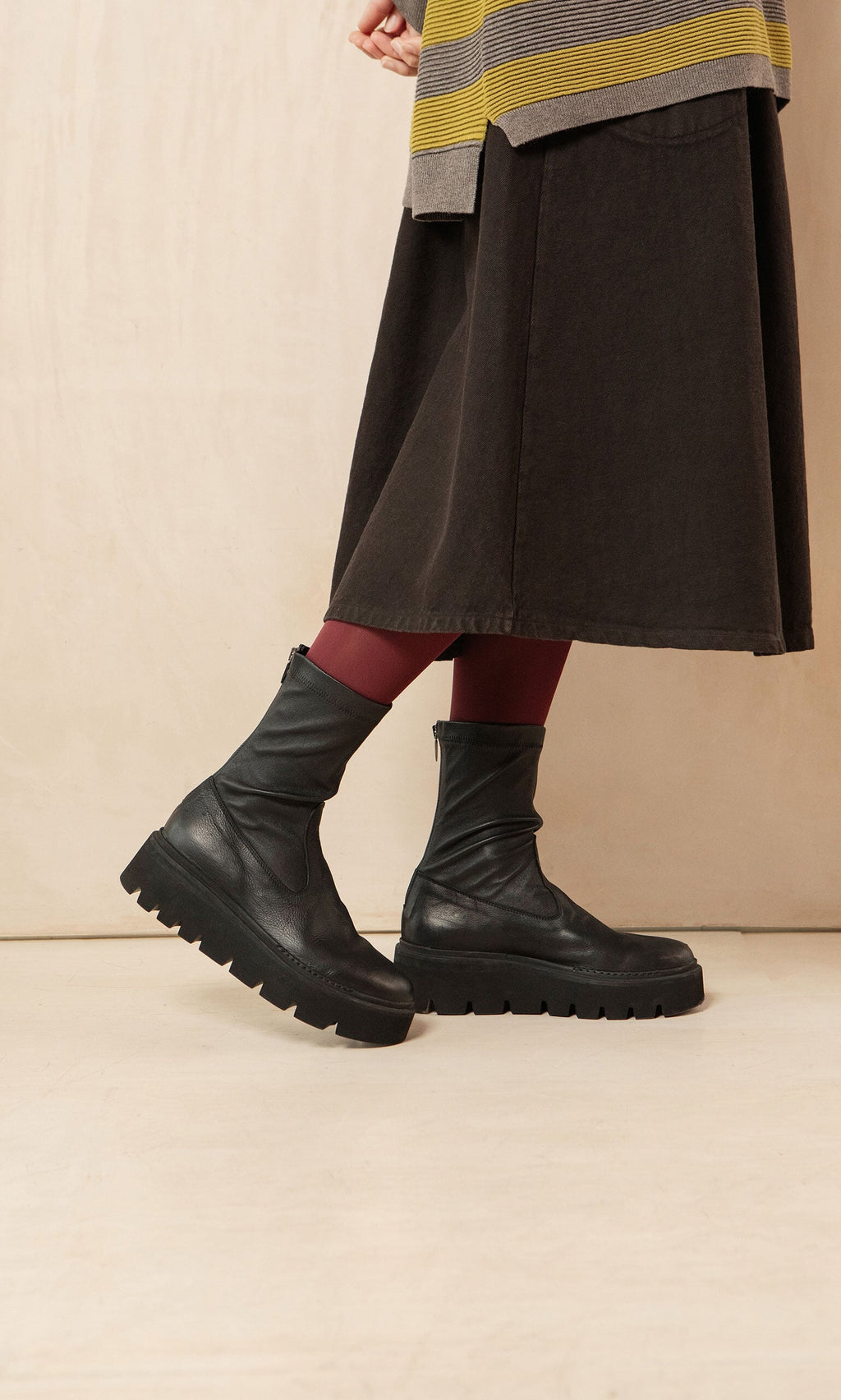 Plümo- Person in a dark skirt, red tights, and Short Prato Boots stands against a beige background.