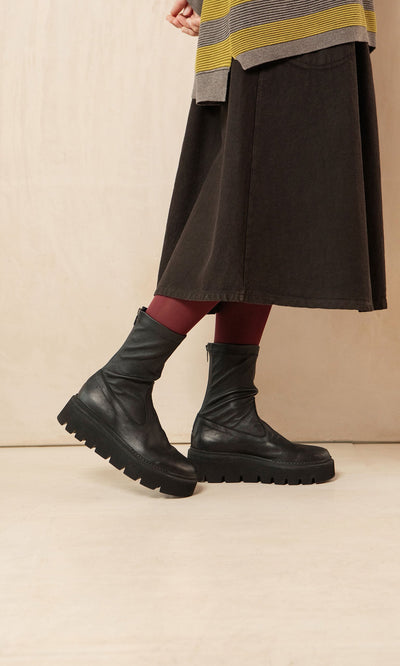 Plümo- Person in a dark skirt, red tights, and Short Prato Boots stands against a beige background.