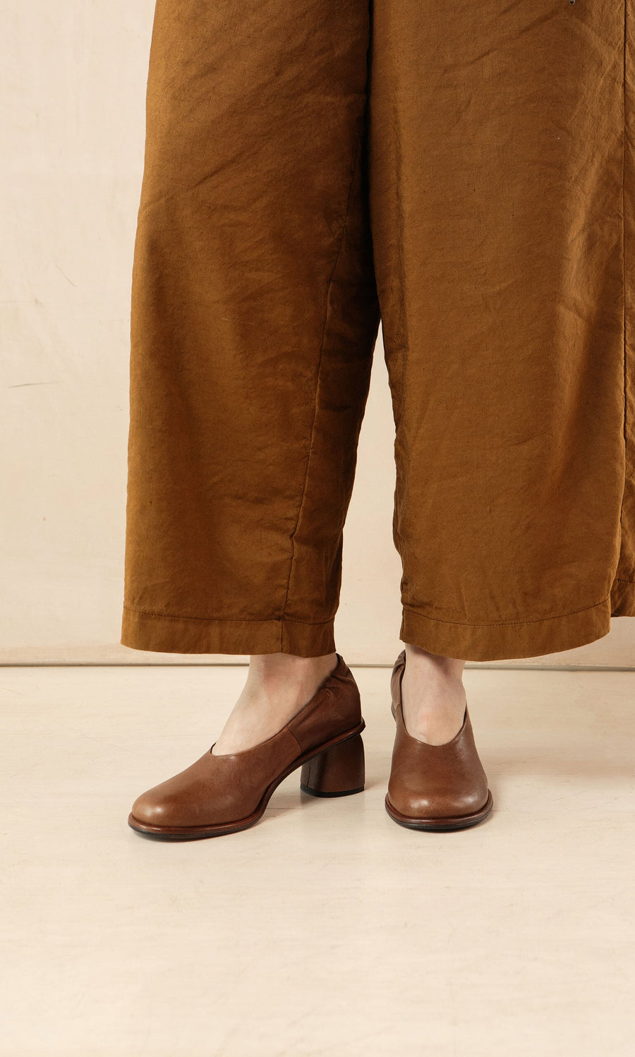 Plümo- Person wearing wide-legged brown pants and Solene Heels, standing on a light-colored floor.