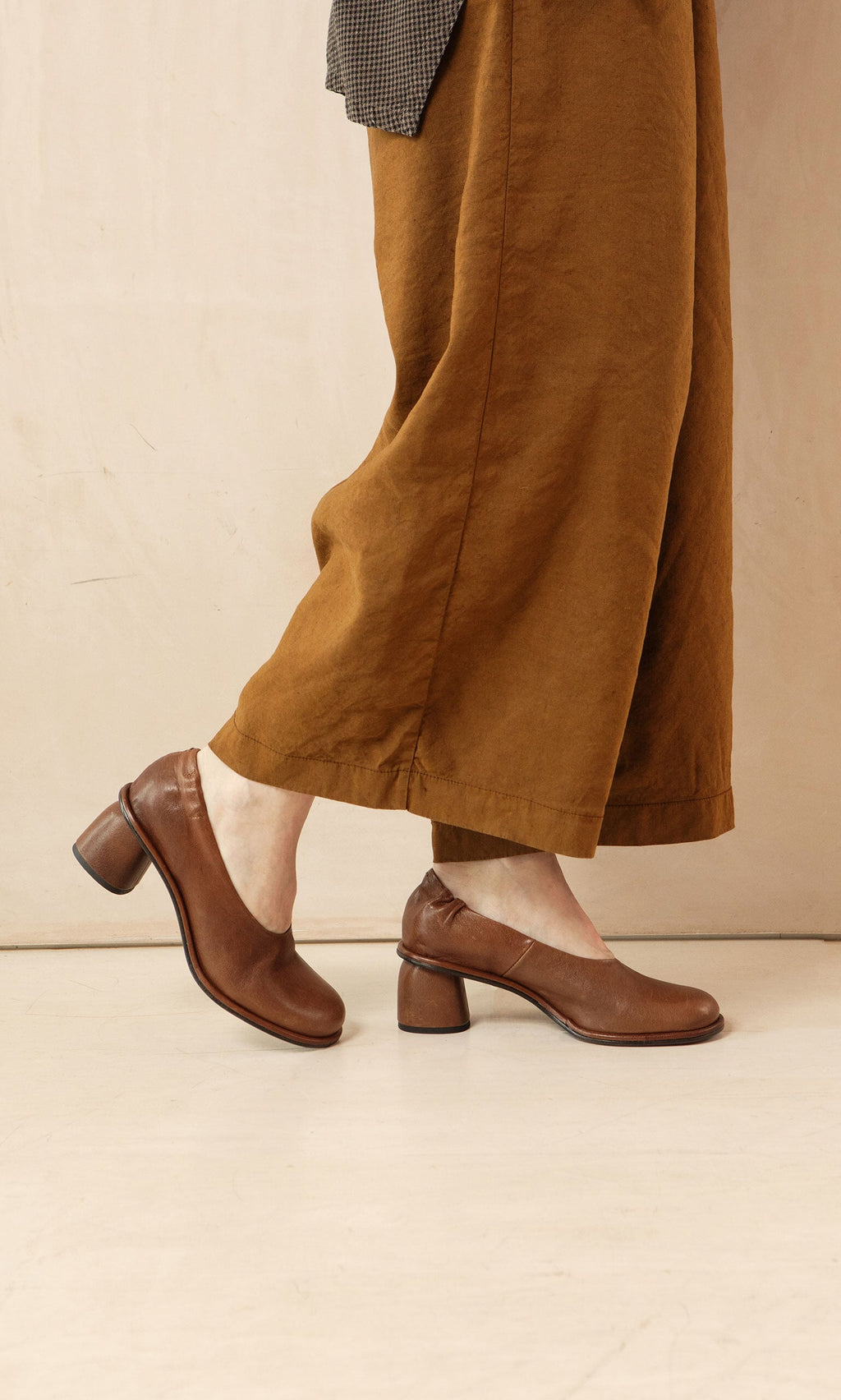 Plümo- Person wearing Kapur Pants with a flattering silhouette and heeled shoes, walking on a light-colored floor.